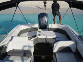 An inviting interior view of a boat featuring comfortable seating and a helm, with two individuals fishing from the deck — perfect for a day of adventure on the water.