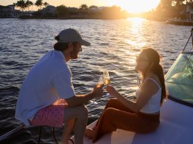 A couple enjoys a romantic toast with cocktails on the deck of a boat at sunset, creating the perfect atmosphere for special moments on the water.