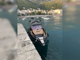 A sleek speedboat docked at the marina, showcasing its stylish design against a picturesque backdrop of mountains and beachside buildings.