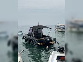 A sleek black boat is docked in calm waters, showcasing its design and structure against a serene backdrop.