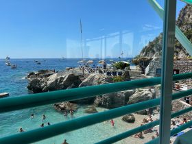 A vibrant beach scene with people swimming in clear waters, surrounded by boats and stunning coastal views — a perfect summer getaway.
