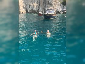 A couple enjoys a refreshing swim in crystal clear waters, with boats anchored nearby, capturing the essence of a perfect summer day on the water.