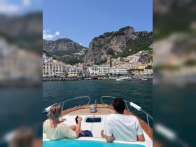A couple enjoys the stunning views of the Amalfi Coast from the bow of their boat, capturing the essence of a perfect day on the water.