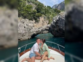 A couple shares a romantic kiss on the bow of a boat, surrounded by stunning coastal scenery — an ideal moment for lovebirds exploring the beautiful waters.