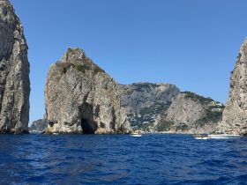 A stunning view of the rugged coastline of Capri, showcasing dramatic cliffs and boats navigating the vibrant blue waters — a perfect destination for scenic boat tours.