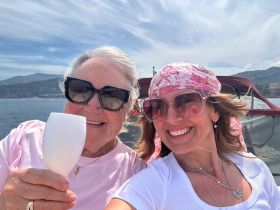 Two women enjoy a joyful moment on a boat, raising their glasses in celebration against a stunning coastal backdrop — perfect for memorable outings and gatherings.