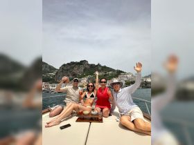 A lively group enjoys cocktails aboard a yacht, celebrating under the sun with stunning coastal views in the background — perfect for memorable outings on the water.