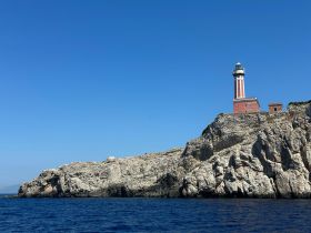 A stunning view of a lighthouse perched on a rocky cliff, surrounded by clear blue waters — a picturesque coastal landmark perfect for sightseeing during boat trips.