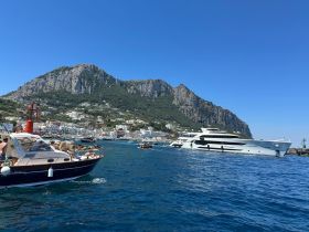A scenic view of a bustling harbor with yachts and boats, set against the stunning backdrop of cliffs and charming coastal buildings — perfect for island hopping adventures.