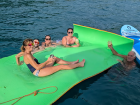 A lively group enjoys drinks and relaxation on a floating mat in the water, capturing the essence of fun and camaraderie during a day on the boat.