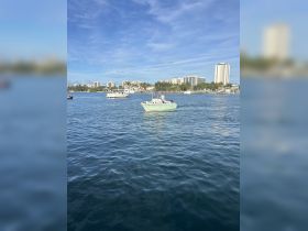 A small boat navigates through calm waters with a vibrant city skyline in the background, showcasing a perfect day for boating adventures.
