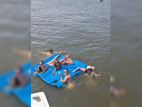 A fun group of friends enjoys a sunny day on a floating mat, sipping drinks and relaxing in the water — the perfect summer getaway.