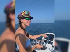 A woman confidently steers a boat while enjoying a sunny day on the ocean, showcasing the thrill of boating adventures.