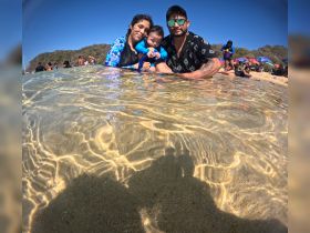 A joyful family enjoys a day at the beach, with a child in their arms, creating lasting memories in the shallow waters.