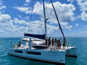 A lively group enjoys a day on the catamaran 'Le Guepard', celebrating under the sun with stunning turquoise waters in the background.