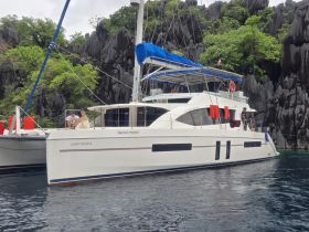 A couple enjoys a moment aboard the catamaran 'Happy Hours II' surrounded by stunning rock formations, perfect for a scenic getaway.