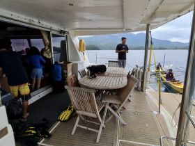Inside view of a spacious boat cabin featuring a dining area and seating, with guests preparing for an adventure on the water.