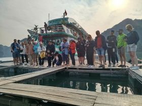 A diverse group of tourists gathers on a dock near the 'Cat Ba Green Trail' boat, engaged in an exciting fishing experience, showcasing the beauty of the Cat Ba region.