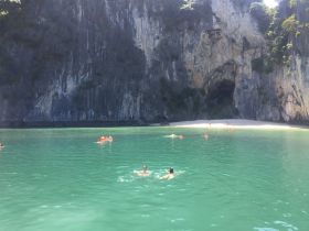 A vibrant scene of swimmers enjoying the clear waters near a stunning cave and beach, perfect for snorkeling and group adventures.