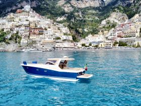 A beautiful boat glides through the turquoise waters near a picturesque coastal town, showcasing the stunning scenery of the Amalfi Coast.