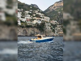 A stylish yacht navigates the stunning coastline, showcasing the beautiful architecture of the Amalfi Coast in the background.
