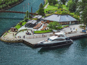 A stunning view of a yacht docked near a bustling waterfront restaurant, surrounded by people enjoying the scenic beauty of the area.