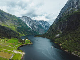 A stunning aerial view of a serene fjord surrounded by majestic mountains, showcasing a boat navigating through the tranquil waters — a perfect representation of Norway's natural beauty.