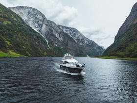 A stunning yacht navigates through a serene fjord, surrounded by majestic mountains and lush greenery — an ideal scene for exploring Norway's breathtaking landscapes.