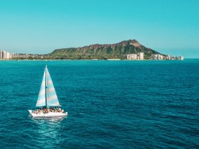 A vibrant sailing experience off the coast of Hawaii, with a group enjoying the stunning views of Diamond Head in the background.