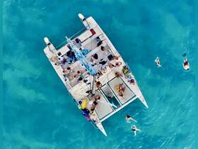 A lively group enjoys a day on a catamaran in stunning turquoise waters, with guests swimming and soaking up the sun — an ideal setting for fun and relaxation.