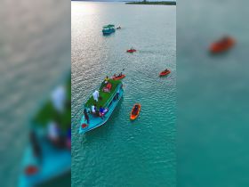 A vibrant scene of guests enjoying kayaking around a colorful boat, showcasing a fun day on the water with friends and family.