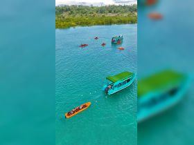 An aerial view captures a vibrant scene of various boats, including kayaks, navigating through crystal-clear waters, showcasing a lively day of water activities.