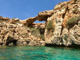 A stunning view of a natural rock formation arching over crystal-clear waters, showcasing the beauty of the coastline — perfect for scenic boat tours and exploration.