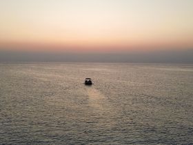 A serene view of a boat cruising across calm waters at sunset, showcasing the tranquility of a perfect evening on the sea.