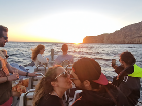 A romantic moment between a couple as they share a kiss while enjoying a sunset cruise with friends — a perfect backdrop for unforgettable memories on the water.