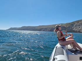 A woman enjoys a relaxing moment on a boat with a drink, surrounded by stunning coastal scenery — perfect for a day of adventure on the water.