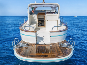 A clear view of the back of a boat, showcasing its elegant design and wooden deck against a vibrant blue ocean backdrop.