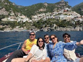 A joyful group of friends enjoys a sunny day on a boat, with stunning coastal views in the background — perfect for memorable outings along the Amalfi Coast.