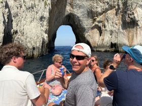 A lively group enjoys a day on the water, celebrating with drinks while exploring stunning coastal rock formations — perfect for memorable boating adventures.