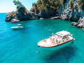 A lively group enjoys a sunny day on a boat, surrounded by stunning turquoise waters and rocky cliffs — perfect for summer adventures and coastal exploration.