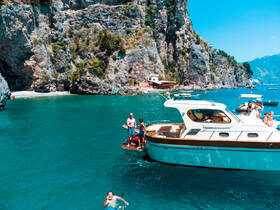 A lively scene featuring a group enjoying a sunny day on the water, with one person swimming and others aboard a boat near a stunning coastal backdrop.