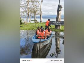 A group of friends enjoys a boat ride on a serene lake, wearing life jackets and surrounded by lush greenery — an exciting adventure in nature.