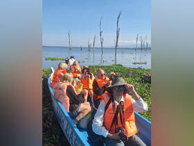 A lively group of adventurers in bright orange life jackets enjoys a boat safari, capturing the scenic beauty around them. Perfect for nature enthusiasts and explorers.