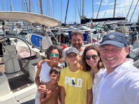 A cheerful family poses for a selfie at the marina, surrounded by boats — a perfect moment capturing the excitement of their upcoming sailing adventure.
