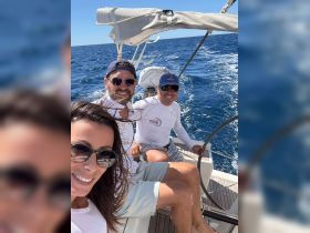 A joyful group of friends enjoys a sailing adventure on the open ocean, capturing the moment with a selfie amidst the beautiful blue waters.