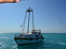A charming boat sails through turquoise waters, with guests enjoying the scenic views — perfect for a day of adventure on the water.