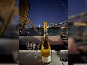 A bottle of wine and two glasses set on a boat's deck at night, with a beautiful bridge illuminated in the background — perfect for a romantic evening on the water.
