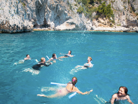 A lively group enjoys a refreshing swim in crystal-clear waters, surrounded by stunning cliffs — perfect for a fun day of water activities and exploration.