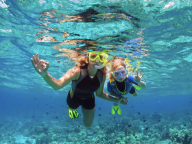 A joyful moment captured underwater as a woman and a child snorkel together, exploring vibrant marine life in crystal-clear waters — a perfect family adventure.