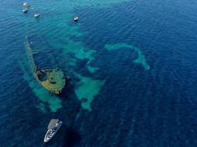 An aerial view captures a sunken shipwreck with snorkelers exploring the vibrant waters, showcasing an exciting underwater adventure.